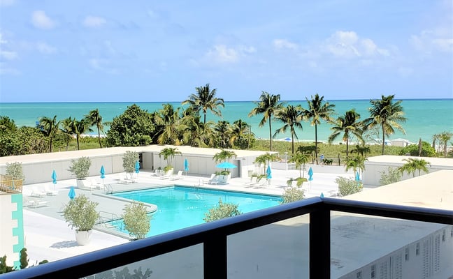 Oceanfront balcony view with pool, beach, and turquoise water below